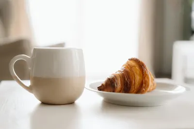 A butter croissant on a plate next to a cup